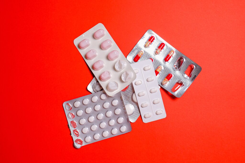 An assortment of pills and capsules in blister packs displayed on a vibrant red surface.