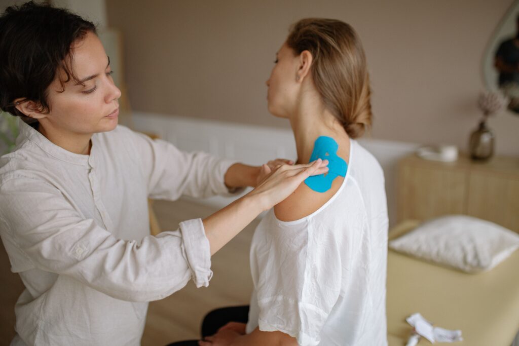 Blogs A physiotherapist applies blue kinesiology tape to a patient's shoulder for muscle support.